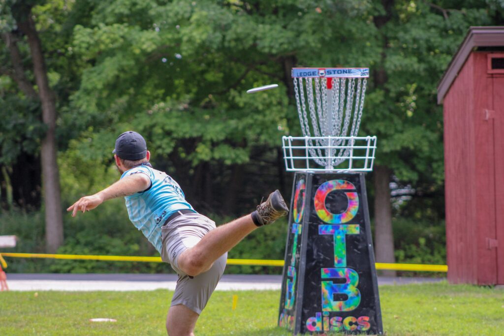 Man playing disc golf outdoors, expertly throwing frisbee towards basket in a lively game.
