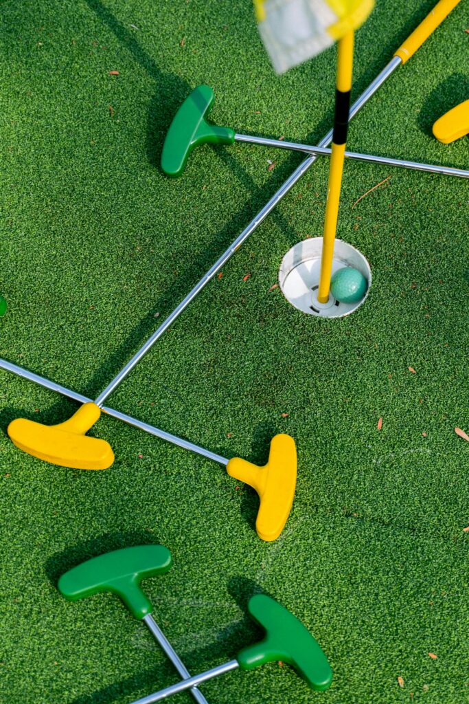 Colorful mini golf putters arranged around a hole on a vibrant green putting surface.
